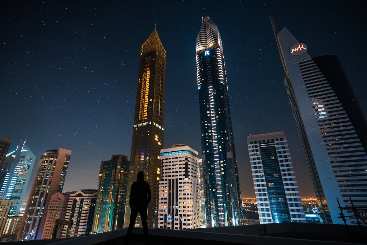 A silhouette stands against the illuminated skyscrapers of Dubai's skyline under a starry night sky.