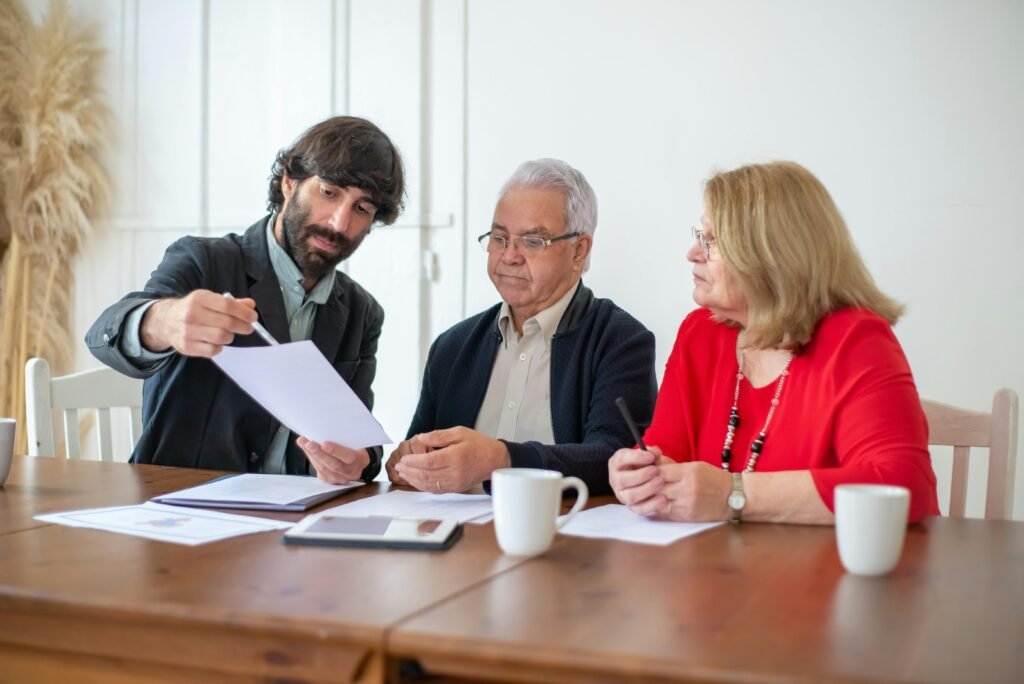 Elderly couple discussing documents with advisor at a wooden table indoors.